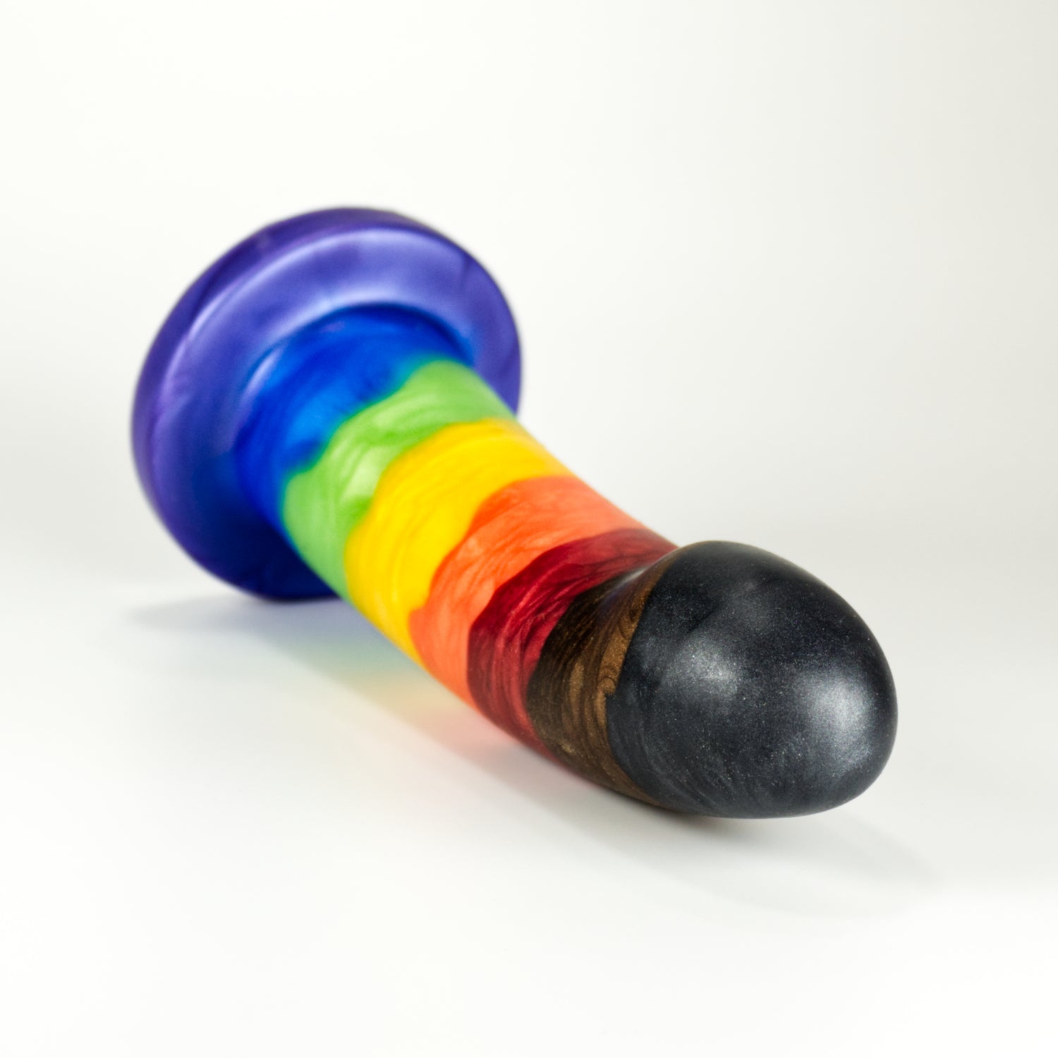 A Sidekick dildo lying down facing the viewer, striped in Intersectional Pride rainbow colors (Rainbow plus black and brown)
