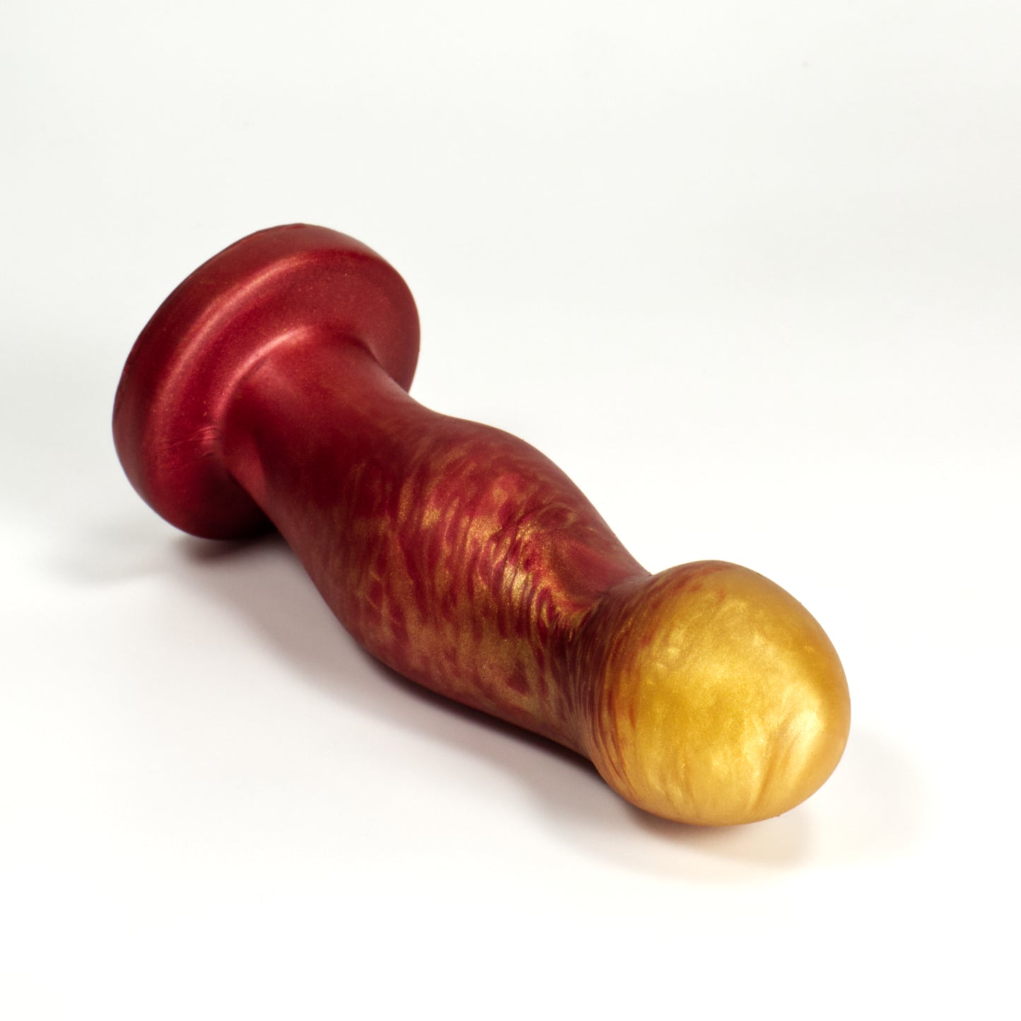 Top view of the Ally Small, a dildo shaped like a curved cylinder that flares out into pronounced bumps at the tip and center of the toy. Each bump has most of its volume towards the front of the toy, a little on the sides, and none on the back, which is smooth. The bumps are somewhat egg shaped.