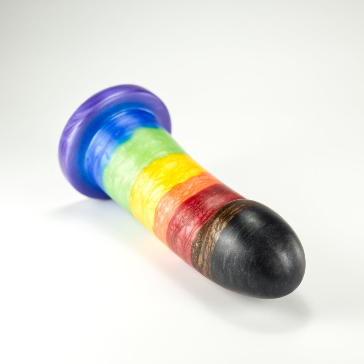 Top view of the Sidekick Large, a dildo with a smooth cylinder shaped body, and a fingertip-shaped tip, and a pronounced cliff shape where they meet. The color is rainbow stripe with additional black and brown stripes at tip.